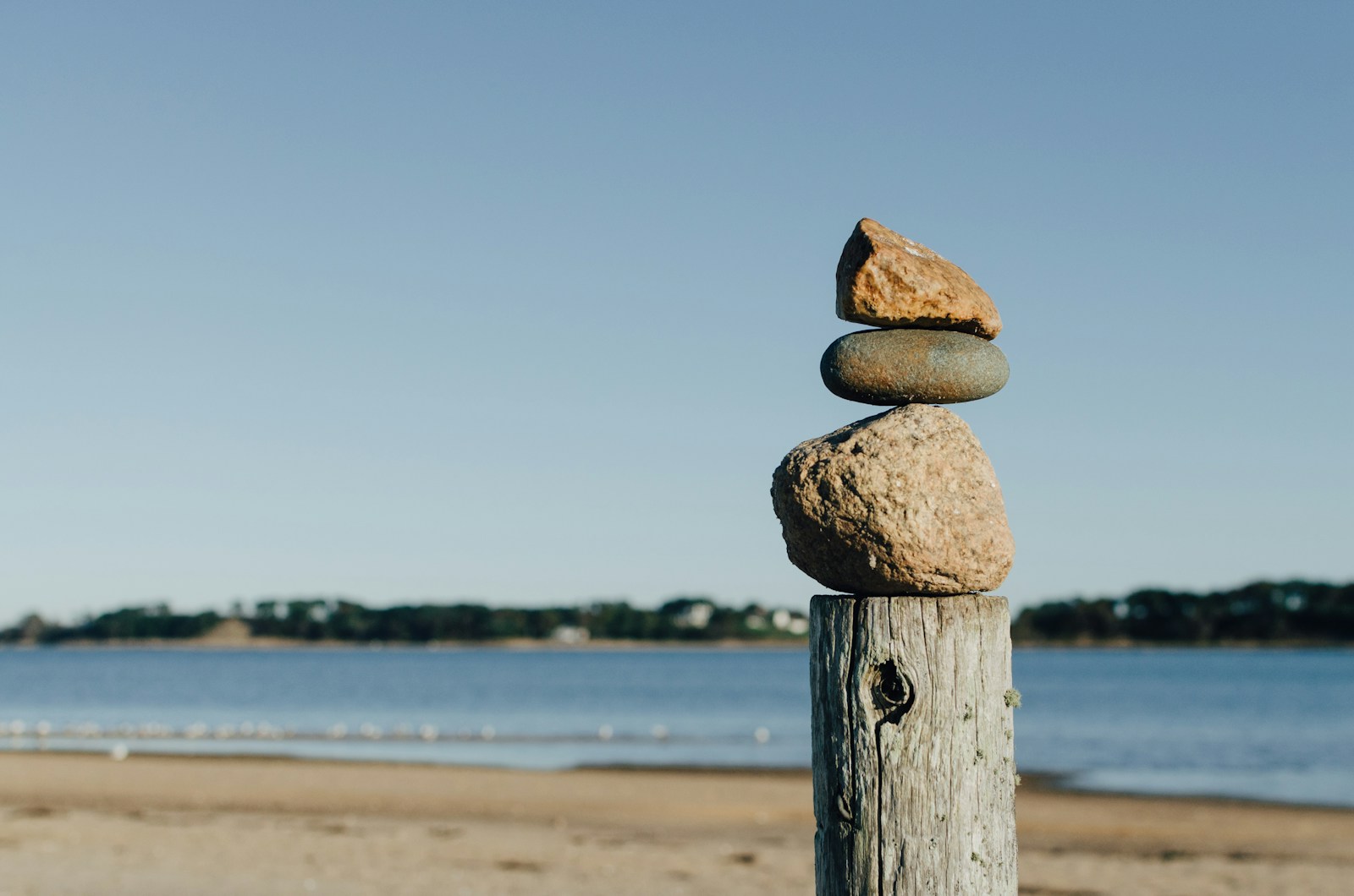 Photo by Kelly Sikkema rock balancing on wooden post near body of water
